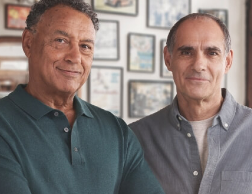 Two older men standing side by side both looking at the camera
